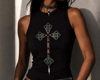 Op de afbeelding: Een zwart mouwloos hemd met een grote kruisafbeelding bestaande uit groene printplaatpatronen en zwarte accenten. Het hemd wordt gecombineerd met een bijpassende zwarte choker met een zilveren kruishanger en een rechthoekige groene printplaat-clutch.