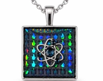 Op de afbeelding: Een vierkante zilveren hanger aan een ketting met een centraal atoom-symbool. Het atoom is geaccentueerd met donkerblauwe kristallen. De achtergrond van de hanger heeft een donker, iriserend rasterpatroon dat groen en blauw licht reflecteert.