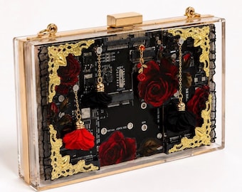 Op de afbeelding: Een rechthoekige clutch van doorzichtig acryl met een zwarte printplaat aan de binnenzijde. Het ontwerp is versierd met donkerrode stoffen rozen, zwarte stoffen kwastjes, goudkleurige metalen hoekstukken en een goudkleurige metalen sluiting.