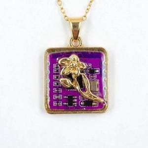 Peut inclure: Pendentif de collier doré avec un design de circuit imprimé violet carré et un accent de fleur dorée. Le pendentif est suspendu à une fine chaîne dorée. La fleur est une conception en trois dimensions.