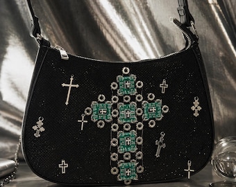 Op de afbeelding: Een zwarte schoudertas met een glinsterende textuur, voorzien van een groot centraal kruis opgebouwd uit groene printplaatvierkanten en zilveren metalen oogjes. De tas is versierd met diverse zilverkleurige kruishangers en hardware.