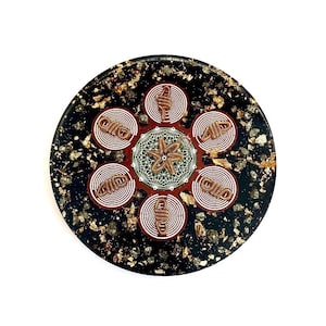 Pode incluir: Uma peça decorativa redonda e preta com flocos dourados e um design central. O design apresenta um elemento em forma de estrela rodeado por seis padrões circulares com espirais de fio de cobre e círculos concêntricos brancos.