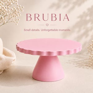Pode incluir: Um suporte para bolos rosa claro com borda recortada e uma base cónica larga. O texto BRUBIA e a frase Small details. Unforgettable moments. aparecem acima do suporte, acompanhados por um pequeno ícone de coração entre duas linhas.