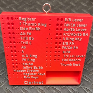 May include: A red 3D-printed clarinet fingering chart with a metal ring for hanging. The chart features labels for various keys and systems, including "Register," "F Thumb Ring," and "Clarinet." The text is in white.