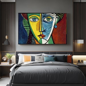 Peut inclure: Peinture de portrait abstrait avec un design de visage divisé. Un côté est jaune et l'autre bleu, avec des accents verts et rouges. L'œuvre est encadrée et exposée au-dessus d'un lit avec une literie grise.