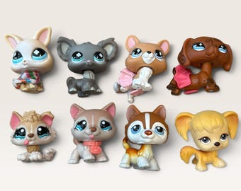 May include: A collection of eight small plastic animal figurines with oversized heads and large blue eyes. The set includes various dog and cat-like characters in shades of brown, gray, tan, and white, some featuring small accessories like collars.