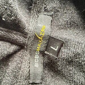 May include: Close-up of dark gray fabric with a tag that reads "BCBGMAXAZRIA" in white and yellow lettering. A smaller tag indicates the size "L". The fabric appears to be a knit or woven material.