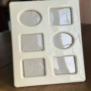 May include: Cream-coloured multi-photo frame with five openings: two oval and three rectangular. The frame has a glossy finish and a smooth surface. The openings are filled with a light grey backing.