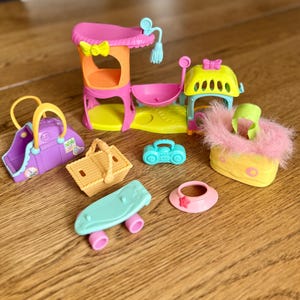 May include: A collection of colorful miniature toys, including a purple handbag, a picnic basket, a teal skateboard, a pink sun hat, and a yellow and pink playset with a bow. A small teal radio and a yellow and pink fluffy purse are also included.