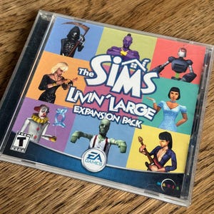 May include: The Sims Livin' Large Expansion Pack CD-ROM. The game case features a colorful design with various character illustrations. The title is prominently displayed with the EA Games logo. The case is in a clear plastic jewel case.