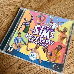 May include: The Sims House Party Expansion Pack CD case. The cover features cartoon characters in various outfits, with the game's title and logo prominently displayed. The EA Games logo is also visible.