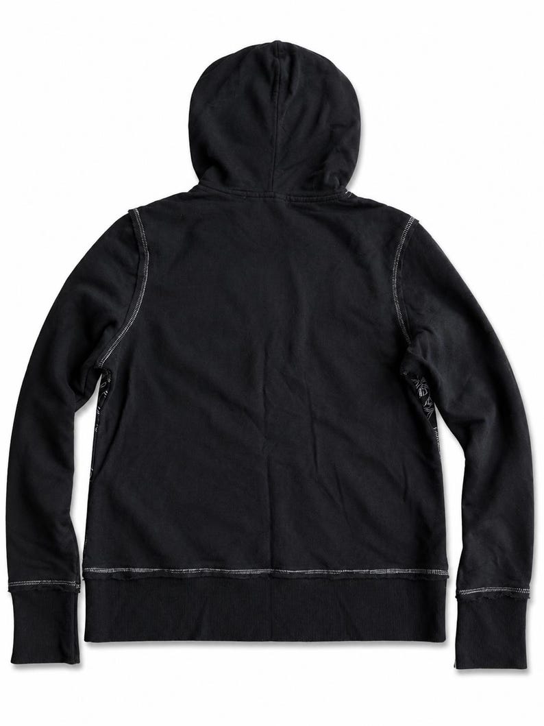 May include: A black hoodie with a hood and long sleeves. The hoodie has white stitching along the seams and cuffs. The back of the hoodie is visible, and the fabric appears to be a soft material.