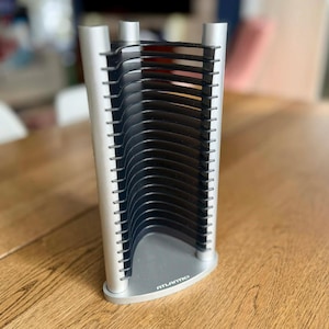 May include: A silver and black CD rack with a triangular base and vertical supports. The rack has multiple slots to hold CDs. The brand name "ATLANTIC" is visible on the base. The rack is made of metal and plastic.