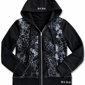 May include: Black zip-up hoodie with a floral design in silver and white. The hoodie features a drawstring hood, front pockets, and the letters "BCBG" embroidered on the hood and lower right side. The zipper is silver.