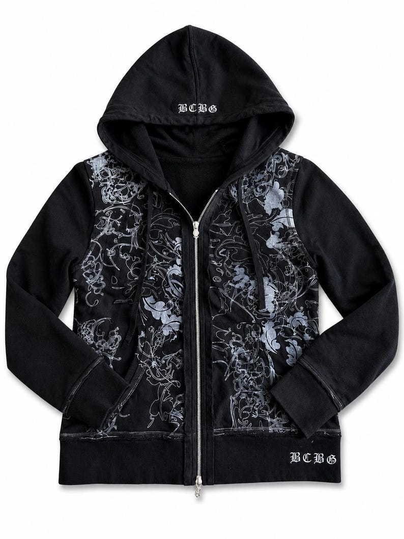 May include: Black zip-up hoodie with a floral design in silver and white. The hoodie features a drawstring hood, front pockets, and the letters "BCBG" embroidered on the hood and lower right side. The zipper is silver.
