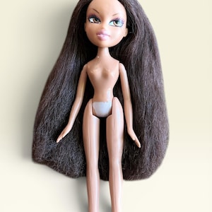 May include: A doll with long, straight dark brown hair, light skin, and large almond-shaped eyes with brown irises. The doll has full pink lips, defined eyebrows, and is wearing white underwear. The figure has articulated arms and legs.