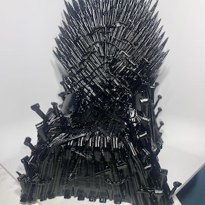May include: A black, 3D-printed Iron Throne replica. The throne is made of numerous swords and spikes, with a glossy finish. The design features a high back and armrests, with a detailed and textured appearance.