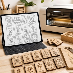 May include: A wooden Mahjong tile set with engraved symbols and characters. A tablet displays a digital version of the tiles. The tiles are arranged on a light-colored wooden surface. A laser cutter is in the background.