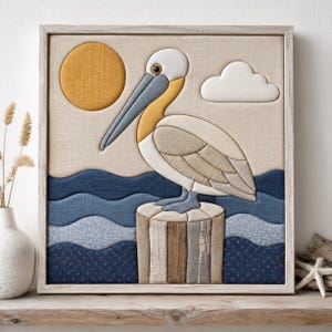 May include: A square framed fabric wall art piece featuring a pelican perched on a wooden piling. The scene includes a yellow sun, a white cloud, and layered blue fabric waves. The pelican is rendered in shades of white, gray, and yellow.