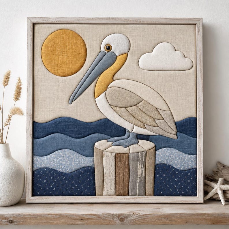 May include: A square framed fabric wall art piece featuring a pelican perched on a wooden piling. The scene includes a yellow sun, a white cloud, and layered blue fabric waves. The pelican is rendered in shades of white, gray, and yellow.