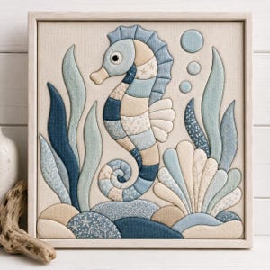 May include: A square framed fabric wall art piece featuring a seahorse in shades of blue, beige, and cream. The seahorse is surrounded by stylized seaweed, a seashell, and bubbles, all constructed from layered fabric patches with various patterns.