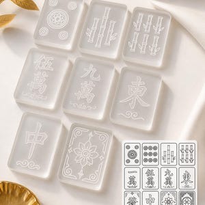 May include: A set of translucent white Mahjong tiles with etched symbols and designs. The tiles feature Chinese characters, bamboo, and flower patterns. A small card displays the tile designs. The game pieces are arranged on a white surface.