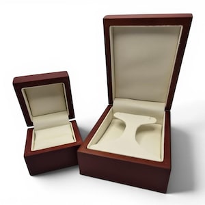 May include: Two open wooden jewelry boxes with a dark reddish-brown finish and cream-colored interior lining. The smaller box features a ring slot, while the larger box includes a T-shaped stand for displaying earrings or other small jewelry items.