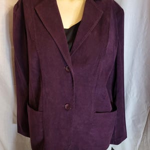 May include: A plum-colored blazer with two front pockets and a two-button closure. The blazer has a notched lapel and is displayed on a mannequin. The blazer is a solid color and appears to be made of a suede-like material. The blazer is a classic style.