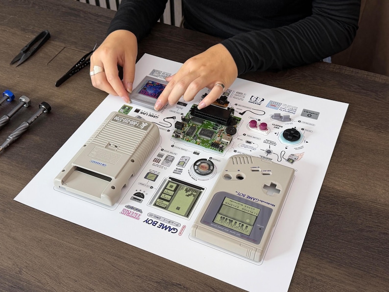 Artist assembling genuine Nintendo Game Boy DMG parts by hand on a precision-printed display template at a wooden workbench – arte hecho a mano, handgemachte Gaming-Deko, handgemaakte gamekunst.