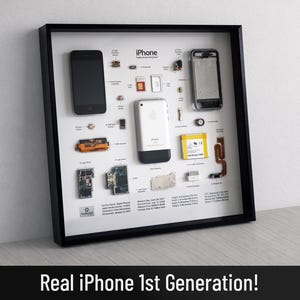 May include: A framed display featuring a disassembled first-generation iPhone with its internal components, including the logic board, battery, and casing, arranged on a white background with labels detailing technical specifications and history.