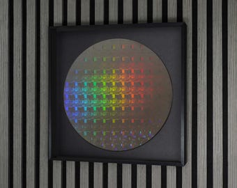 May include: A circular silicon wafer featuring a grid of integrated circuits with a holographic rainbow diffraction pattern, mounted inside a square black frame. The surface displays a repeating geometric pattern that reflects light in spectrum colors.