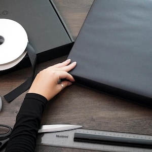 Premium black gift wrapping being prepared by hand for a framed Nintendo Game Boy artwork, suitable as a retro gamer birthday or anniversary gift – regalo gamer, Geschenk für Gamer, cadeau voor gamer.