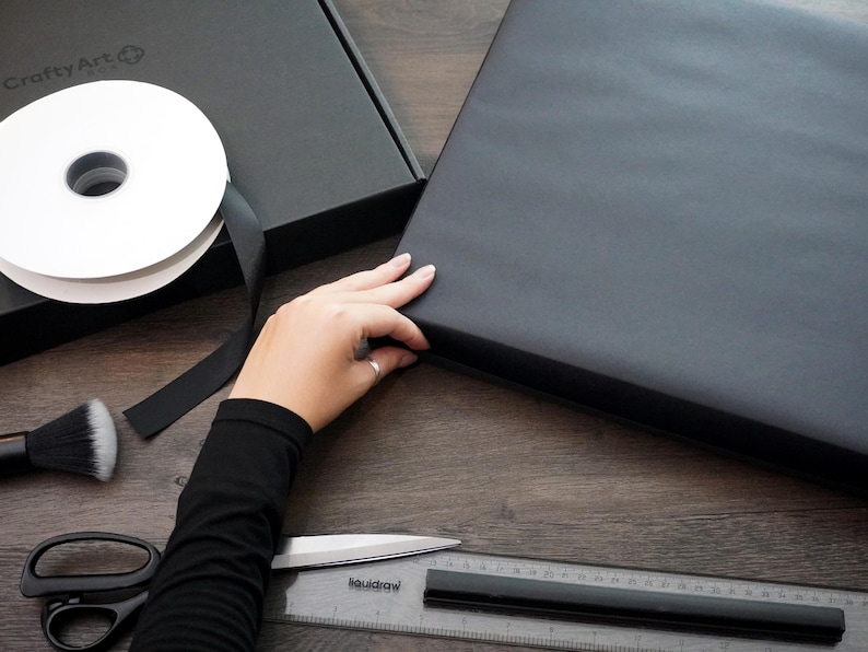 Premium black gift wrapping being prepared by hand for a framed Nintendo Game Boy artwork, suitable as a retro gamer birthday or anniversary gift – regalo gamer, Geschenk für Gamer, cadeau voor gamer.