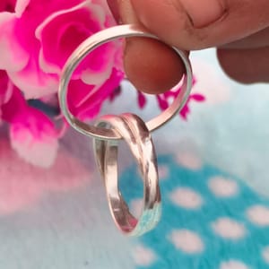 Könnte beinhalten: Zwei silberne Ringe, einer mit einem gedrehten Design, werden vor einem Hintergrund aus rosa Blumen und einer blau-weiß gemusterten Oberfläche gehalten. Die Ringe sind glänzend und reflektieren das Licht, wodurch ihre polierte Oberfläche zur Geltung kommt. Der Fokus liegt auf dem Schmuck.