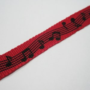 May include: Red ribbon with black musical notes printed on it.
