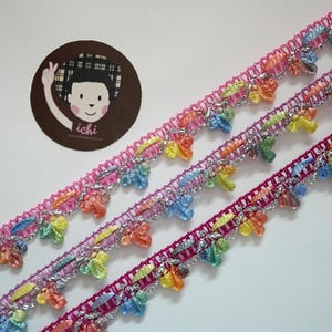 May include: Three strands of colorful trim with silver thread and rainbow-colored fringe. The trim is pink, purple, and red.