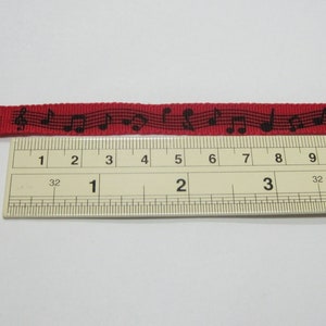 May include: Red ribbon with black musical notes printed on it. The ribbon is measured against a ruler, showing it is approximately 4 inches long.