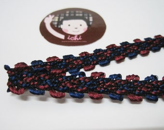 May include: A close-up of a dark blue and burgundy braided trim with a textured pattern. The trim has a scalloped edge and is made of a soft, woven fabric.