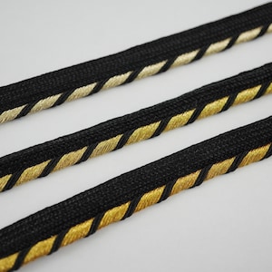 May include: Black and gold trim with a braided design. The trim is made of a soft, woven fabric and has a subtle sheen.