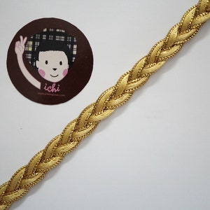 Puede incluir: Borde trenzado dorado con un brillo sutil. El borde está tejido en un patrón de trenza y tiene una textura delicada.