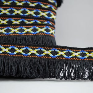 May include: Black trim with a fringe and a geometric pattern in orange, blue, white, and yellow.