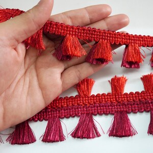 Puede incluir: Borde de flecos rojo y burdeos con base tejida. El borde tiene una franja de flecos a ambos lados.