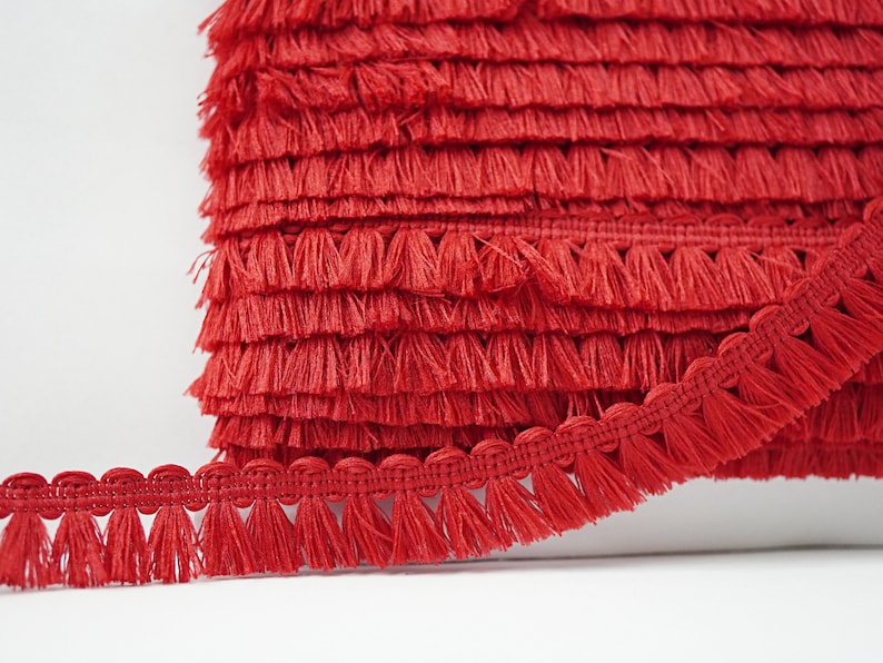 May include: Red tassel trim with a scalloped edge. The trim is made of soft, fluffy yarn and is perfect for adding a touch of whimsy to any project.