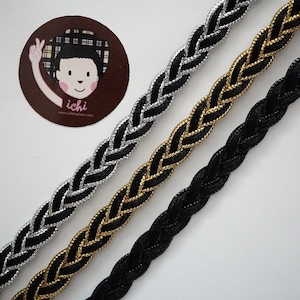 May include: Three braided trim cords in black, gold, and silver. The cords are woven with a simple braid pattern.