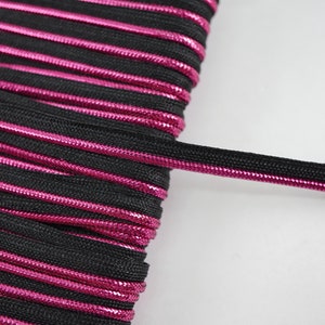 May include: Black and pink elastic cord with a metallic sheen. The cord is coiled and a single strand is extended.