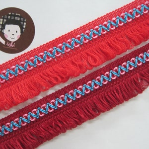 May include: Red fringe trim with a blue and pink geometric pattern. The trim has a soft, fluffy texture and is perfect for adding a touch of elegance to any project.