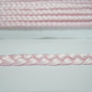 May include: A close-up of a pink braided cord. The cord is made of a soft, silky material and has a delicate, feminine look.