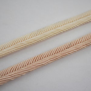 Puede incluir: Dos piezas de ribete trenzado, una en color crema claro y la otra en color melocotón pálido. El ribete tiene un patrón de espiga.