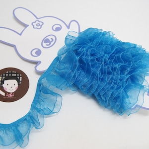 Op de afbeelding: Een turquoise blauwe gerimpelde trim met een glinsterende afwerking. De trim is gemaakt van een zachte, doorschijnende stof en is perfect om een ​​toets van elegantie aan elk project toe te voegen.