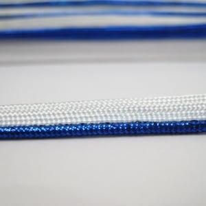 May include: White and blue cord with a metallic blue trim. The cord is made of a woven material and has a smooth texture.